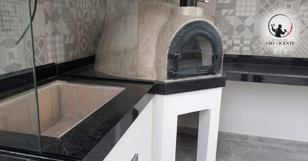 Bancada em granito preto em área gourmet com forno de pizza